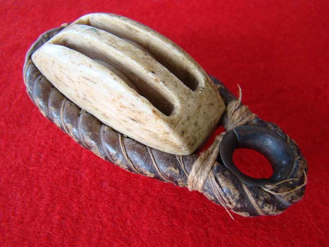 A carved whalebone double block with leather covered rope and brass grommet circa 1850-1870